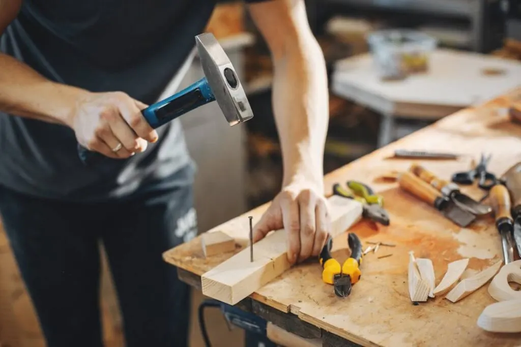 A person using a hammer to drive a nail into a wooden plank.