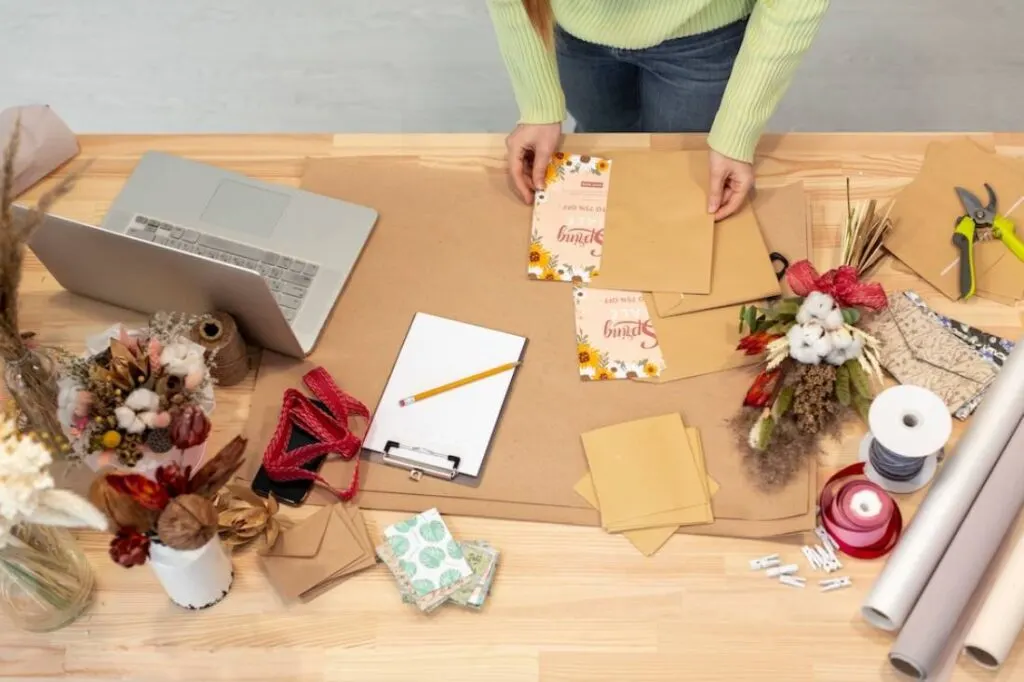 A person arranges crafting supplies on a wooden table.
