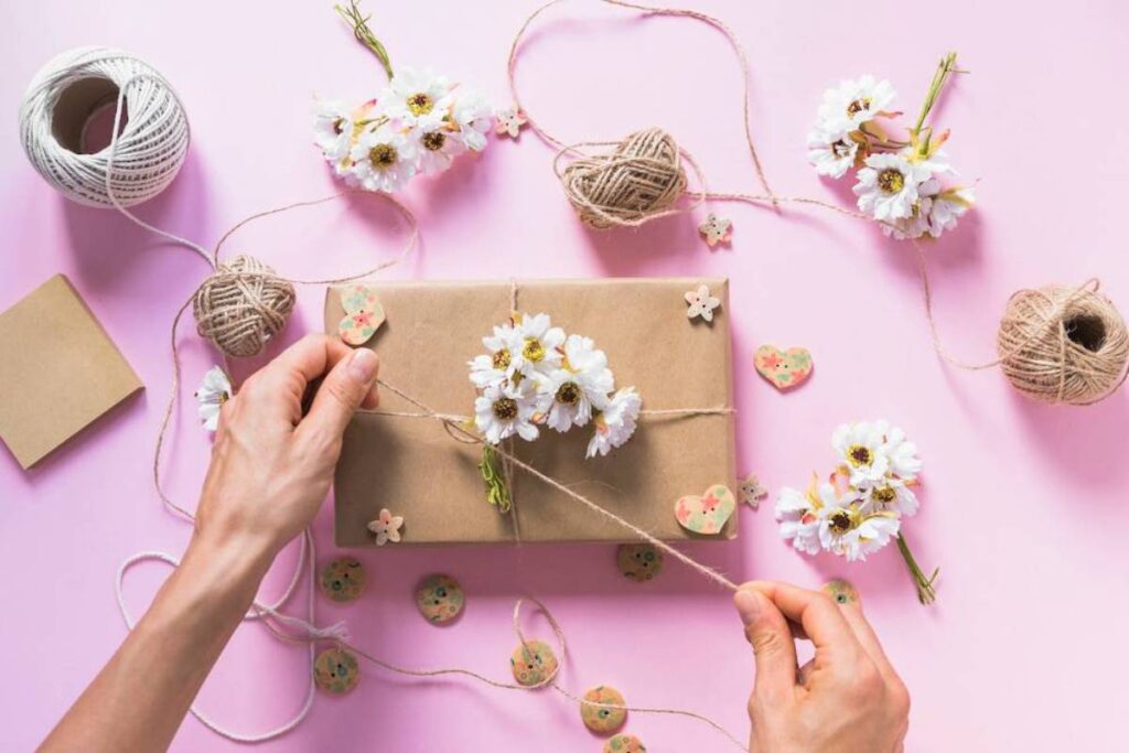 A hand ties twine around a gift wrapped in brown paper.