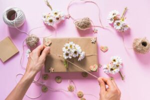 A hand ties twine around a gift wrapped in brown paper.