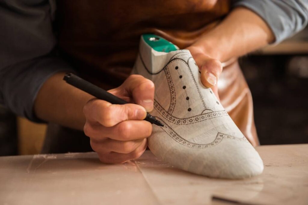 A craftsman detailing a shoe prototype with a marker