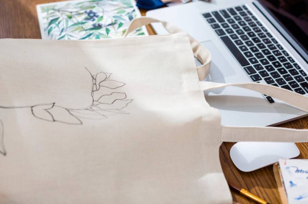 A beige tote bag with a floral outline sits beside a laptop.