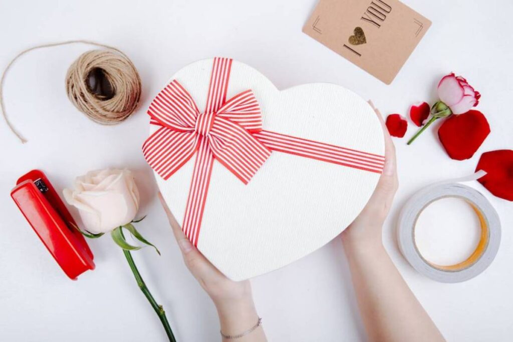 A person holds a heart-shaped gift box with a red ribbon.