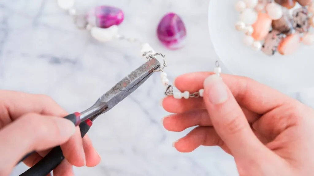 A person's hand holds pliers while fixing a beaded necklace