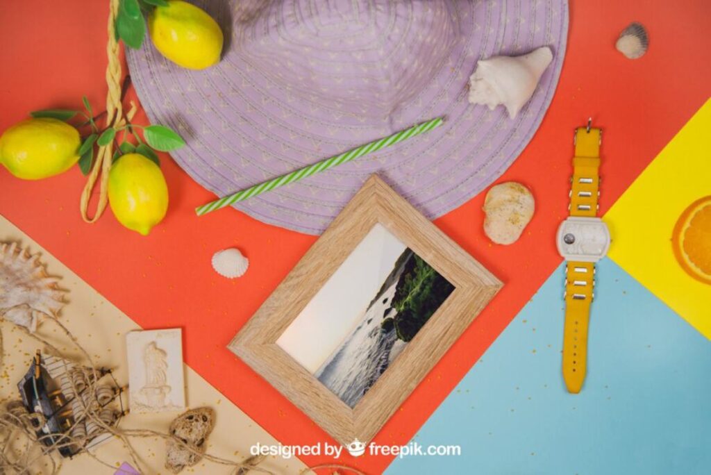 A colorful summer flat lay featuring a lavender hat, lemon, seashells, a photo frame, and a yellow watch on vibrant backgrounds.